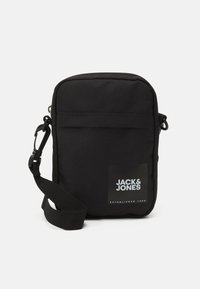 Sac à bandoulière noir en tissu durable. Dispose d'une poche avant, d'une sangle réglable et d'un patch logo avec "JACK & JONES."