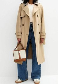 Beige trench coat with a double-breasted design, paired with dark blue wide-leg jeans. Brown and beige structured handbag with a clasp.