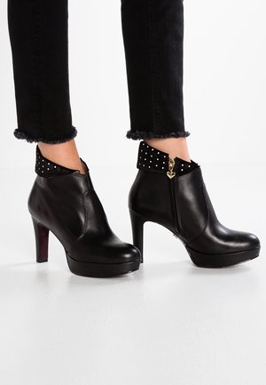 Schwarze Stiefeletten aus Leder mit hohen Absätzen und Plateausohlen, umgeschlagener Manschette mit weißen Nieten und Reißverschluss an der Seite mit herzförmigem Zuggriff.