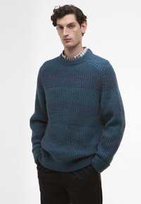 Τυρκουάζ πλεκτό πουλόβερ με υφή, που διαθέτει στρογγυλή λαιμόκοψη και πλεκτές μανσέτες, φορεμένο πάνω από πουκάμισο με καρό σχέδιο, συνδυασμένο με μαύρα παντελόνια.