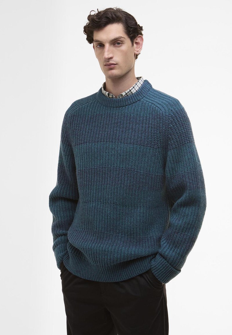 Τυρκουάζ πλεκτό πουλόβερ με υφή, που διαθέτει στρογγυλή λαιμόκοψη και πλεκτές μανσέτες, φορεμένο πάνω από πουκάμισο με καρό σχέδιο, συνδυασμένο με μαύρα παντελόνια.