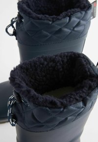 Bottes imperméables de couleur marine avec texture matelassée en haut, doublure en polaire et lacets réglables. section inférieure en caoutchouc lisse pour la durabilité.