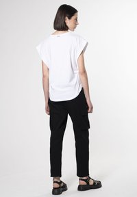 Hvid oversized t-shirt med korte ærmer, kombineret med sorte cargo bukser og kraftige sorte sandaler med justerbar rem.