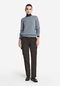 Maglione lavorato a maglia azzurro chiaro con scollo a costine, abbinato a pantaloni cargo in suede scuro con tasche laterali e cintura. A completare l'outfit ci sono delle scarpe nere.