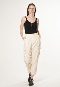 Top nero senza maniche con bordi a scallop e dettagli con bottoni, abbinato a pantaloni cargo crema con molteplici tasche e una vestibilità rilassata. Sandali neri.