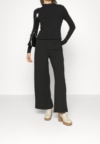 Top noir à manches longues côtelé avec un col rond, associé à un pantalon noir à jambes larges et des chaussures plates-formes beiges. Un sac à main noir brillant est inclus.