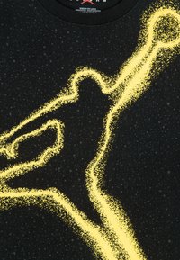 Zwart T-shirt met een geel, gestructureerd beeld van een hand in beweging, met een gespikkeld patroon over de hele stof.