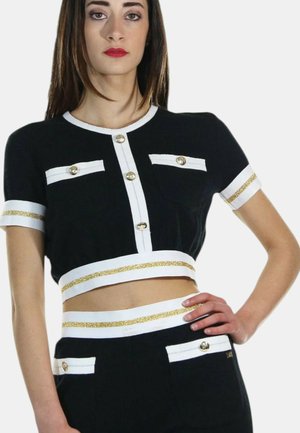 Top corto nero con accenti bianchi, dotato di bottoni dorati e polsini a righe dorate. Include due tasche frontali con dettagli a bottone.