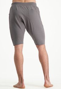 Shorts de sport gris avec un design de couture incurvée, une taille élastique et une petite poche à l'arrière. Matériau léger, coupe à mi-genou.