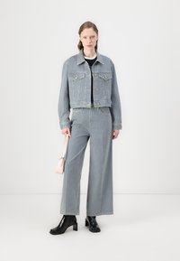 Blå og hvit stripete denimjakke og vide bukser kombinert med svarte ankelstøvletter. Modellen holder en liten rosa håndveske.