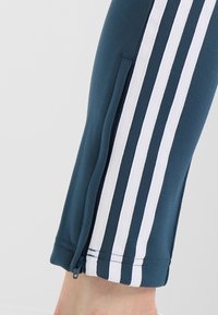 Blå sportbyxor med vita vertikala ränder, en dragkedjeförsedd sidoficka och en tight passform vid vristen. Mjuk textur.