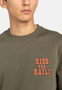 Sudadera verde oliva con cuello de canalé, que presenta un atrevido gráfico en naranja que dice "RIDE THE RAILS" en la parte frontal. Material de algodón suave.