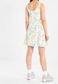 Robe fleurie avec un fond blanc et des fleurs jaunes et bleues, sans manches, jupe évasée et tissu léger.