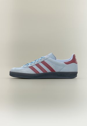 Jasnoniebieski but sportowy Adidas Gazelle z bordowymi paskami, bordową patką na pięcie i czarną podeszwą, pokazany z boku na jednolitym tle.