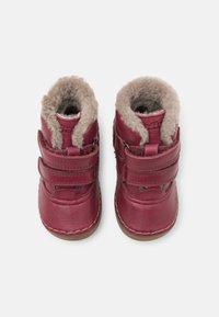 Stivaletti rossi in pelle per bambini, rivestiti in pile beige, con due cinturini in velcro e suole beige cucite, mostrati dall'alto su sfondo bianco.