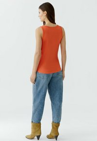 Oranje geribde tanktop gecombineerd met lichtblauwe, loszittende spijkerbroek en beige enkellaarsjes. Heeft een ronde halslijn en een mouwloos ontwerp.