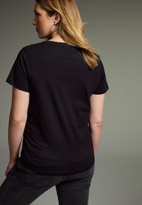 Svart, kortärmad t-shirt gjord av mjukt tyg. Har en standard rund halsringning och en figurnära passform. Bärs tillsammans med mörka jeans.