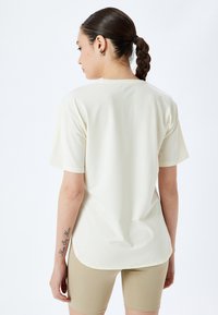 Løs siddende, cremet t-shirt med korte ærmer, rund kant og glat tekstur. Stylet med beige shorts.