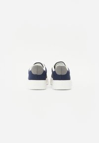 Zapatillas de malla marinas con un capuchón de tacón gris texturizado y suela blanca, con un branding mínimo en la parte trasera y un diseño elegante.