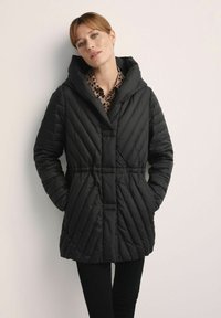 Czarna pikowana kurtka z kapturem, z diagonalnym wzorem pikowania, zawiązywanym w talii oraz zapinana na zatrzaski. Noszona na wzorzystą bluzkę.