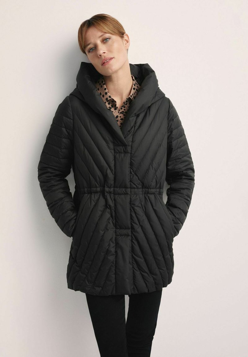 Czarna pikowana kurtka z kapturem, z diagonalnym wzorem pikowania, zawiązywanym w talii oraz zapinana na zatrzaski. Noszona na wzorzystą bluzkę.