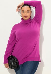 Maglione a collo alto magenta in un morbido tessuto a maglia aderente con maniche lunghe, abbinato a jeans scuri e una borsa nera a pieghe.