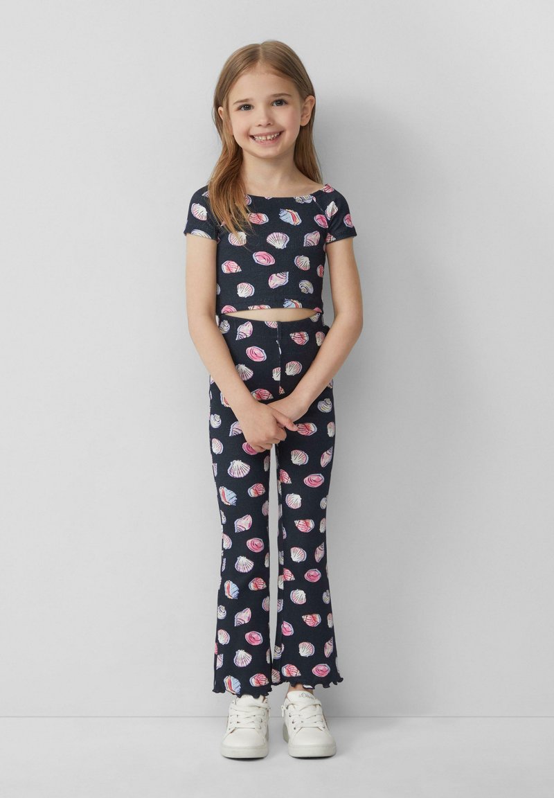 Marineblauw tweedelig outfit met schelppatronen; cropped top met korte mouwen, flared broeken met golfranden. Gecombineerd met witte sneakers.