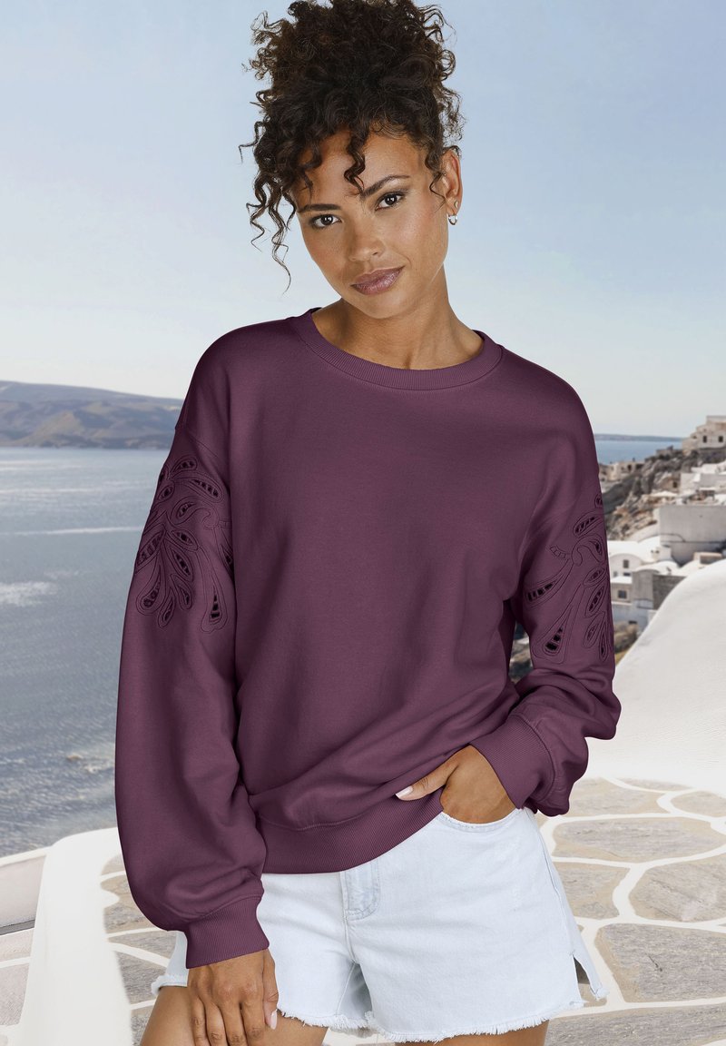 Sudadera burdeos con diseño de recortes intrincados en las mangas, puños y dobladillo acanalados, combinada con pantalones cortos de mezclilla claros.