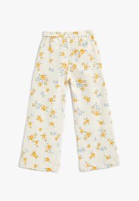 Pantalons à imprimé floral avec un fond crème, ornés de fleurs jaunes et bleues, au design à jambes larges et avec une poche arrière. Tissu texturé.