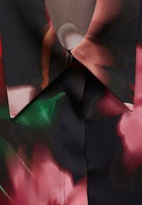 Blouse en soie fleurie avec un fond noir agrémenté de motifs abstraits roses et verts, un col pointu et une texture lisse.