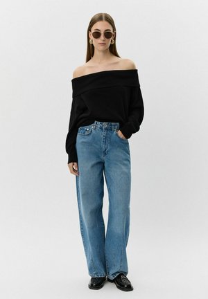 Crna off-shoulder džemper, svijetloplave široke traperice, okrugle sunčane naočale, zlatne naušnice i crne cipele. Glatka tkanina s ležernim krojem.