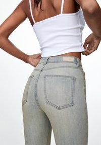 Vaqueros de mezclilla azul claro con un diseño de cintura alta, que presentan dos bolsillos traseros y una pequeña etiqueta de marca en la cintura. Textura suave.