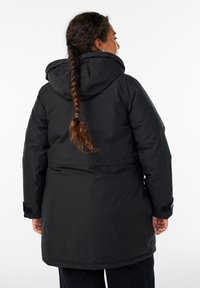 Crna zimska jakna s kapuljačom, koja ima elegantan dizajn i teksturiranu tkaninu. Manžetne imaju podesive kopče, što osigurava čvrsto prianjanje.