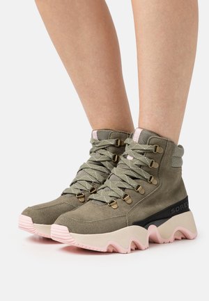 Khaki Wildlederstiefel mit pinker Außensohle, ausgestattet mit metallischen Ösen, gestreiften Schnürsenkeln und einem strukturierten Design. Schickes, hoch geschnittenes Silhouette.
