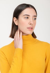 Gelber Rollkragenspullover aus Strickstoff mit gerippten Bündchen und Kragen. Das Design zeichnet sich durch eine enge Passform und eine glatte Textur aus.