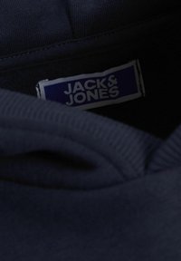 Mörkblå sweatshirt med krage och etikett som visar "JACK & JONES" i vit text mot en blå bakgrund, med sydda ribbdetaljer.