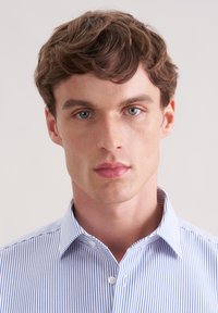 Camicia a righe blu e bianche con bottoni e colletto aperto. Tessuto dalla texture liscia, design aderente, piccolo dettaglio con logo sul petto.