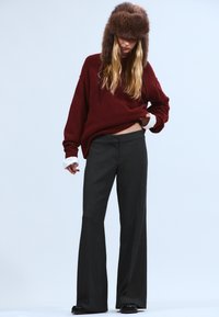 Pull oversized bordeaux, pantalon large gris, et un chapeau en fourrure marron. Matériaux texturés avec coupe ample et manches superposées contrastantes.