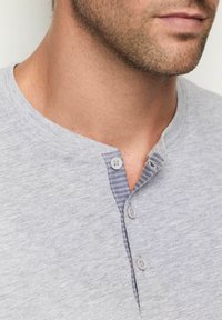 Camisa henley de algodón gris con un cuello redondo y tres botones, con un detalle a rayas en la tapeta. Textura suave.