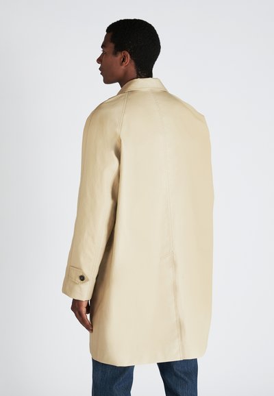 Manteau en cuir beige avec un col et des manches longues, comportant des détails cousus et une coupe droite, associé à un jean en denim.