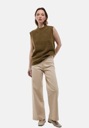 Pull sans manches vert olive en tricot avec un col rond, associé à un pantalon large beige clair et des chaussures neutres. Fond uni.