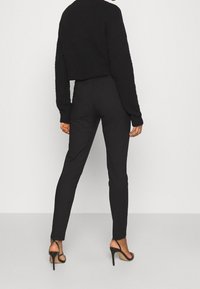 Czarne spodnie z wysokim stanem o dopasowanym kroju i gładkiej tkaninie, zestawione z krótkim, miękkim czarnym swetrem oraz czarnymi sandałami na wysokim obcasie z paskami.
