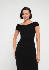 Μαύρο φόρεμα χωρίς ώμους με σφηκοφωλιά λεπτομέρειες, εφαρμοστή σιλουέτα και απαλό, υφασμάτινο υλικό με υφή. Μακρύ σχέδιο μέχρι τον αστράγαλο.