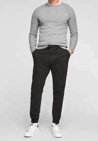 Šedý pletený svetr s kulatým výstřihem, v kombinaci s černými zúženými kalhotami s tkaničkovým pasem a žebrovanými náplety, doplněný bílými teniskami.