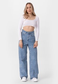 Lichtblauwe denim broek met wijde benen en sterrenpatroon, hoge taille en vijf zakken. Gepaard met een witte cropped top met lange mouwen.