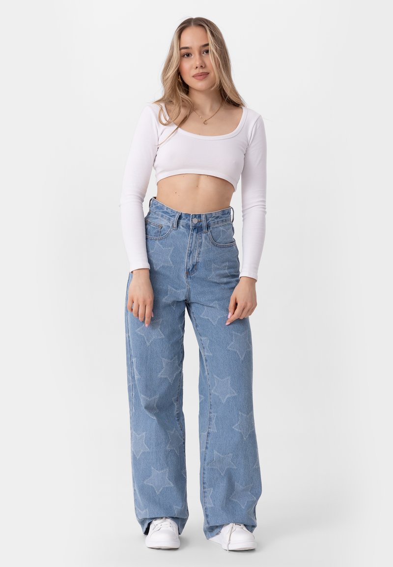 Lichtblauwe denim broek met wijde benen en sterrenpatroon, hoge taille en vijf zakken. Gepaard met een witte cropped top met lange mouwen.
