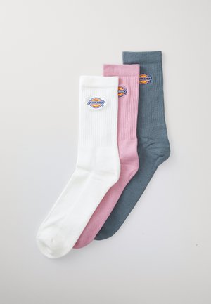 Tres pares de calcetines de crew con canalé en blanco, rosa y gris oscuro, cada uno con un parche circular de marca.