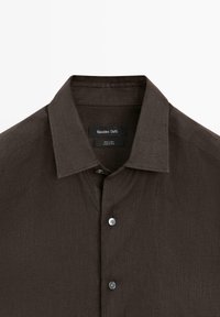 Camicia in lino marrone scuro a maniche lunghe con colletto appuntito e due bottoni visibili, etichettata Massimo Dutti, Made in China.