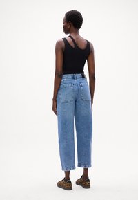 Top de tirantes de canalé negro, jeans de tiro alto de color azul claro, estilo acampanado recortado, con bolsillos traseros, combinados con zapatillas de animal print.
