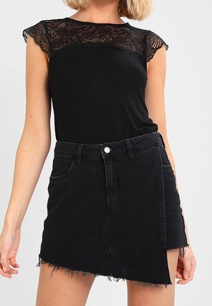 Vrouw die een zwarte kanten top met kapmouwtjes en een asymmetrische zwarte denim minirok met rafelige zoom draagt.